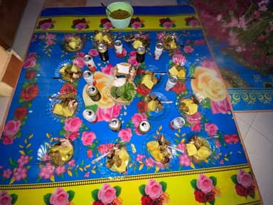 Plates of food, candles and drinks set out on a flowered mat for All Souls' Day in Timor-Leste