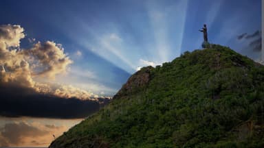 Sun rays behind the Cristo Rei statue on its green headland above Dili