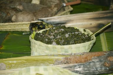 Cooked greens in a woven palm-leaf basket on banana leaves at a village gathering in Baucau