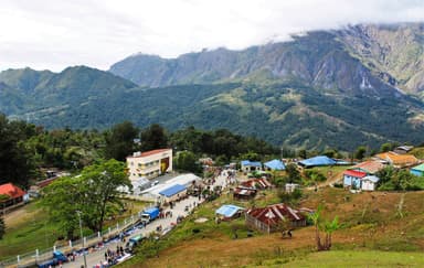A highland village with colourful roofs below forested mountains in Hatu-Builico