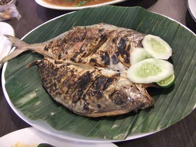 A whole grilled fish on a banana leaf with sliced cucumber
