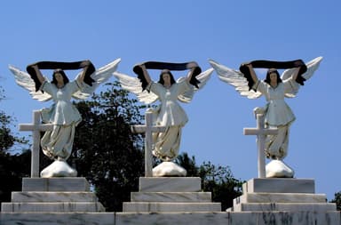 Angel statues holding black ribbons above crosses at Santa Cruz Cemetery, Dili