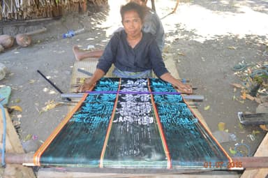 A woman weaving a blue and black tais on a backstrap loom in Oecusse