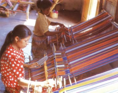 Two women weaving brightly striped tais cloth on looms in Lospalos